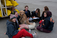 Women rowers sit on ground, with dog Women rowers sit on ground, with dog